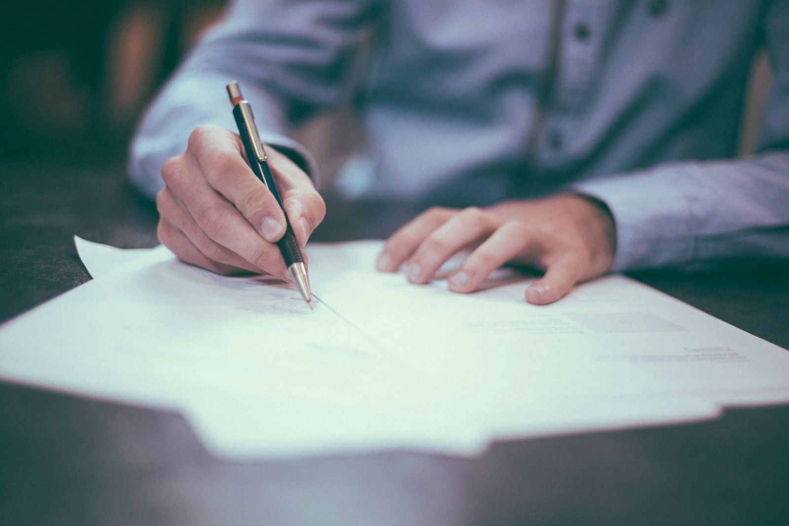 main d'un homme qui écrit au stylo sur des feuilles de papier