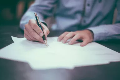 main d'un homme qui écrit au stylo sur des feuilles de papier