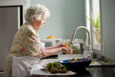 femme âgée nettoyant des légumes à l'évier
