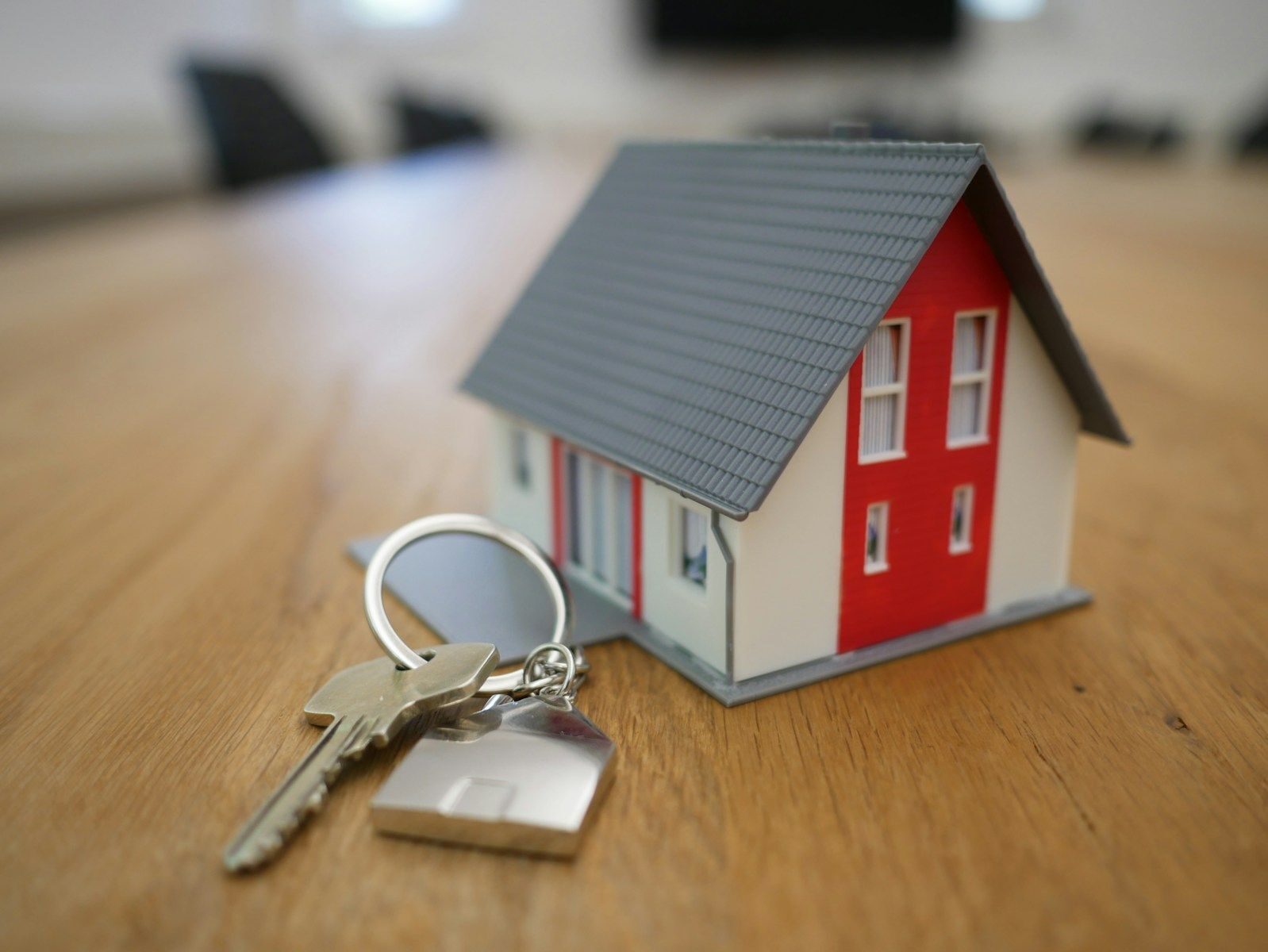 maison miniature rouge posée sur une table avec des clés posées à côté